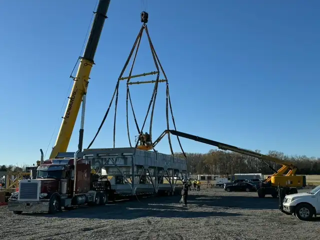 Crane lifting an equipment skid off a truck with a spreader bar